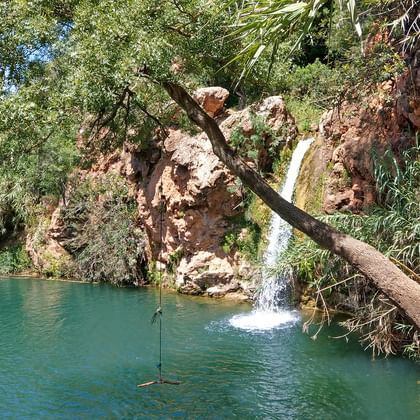 Vattenfall Pego do Inferno som faller ner i en turkos pool omgiven av röda klippor och frodig vegetation i Algarve.