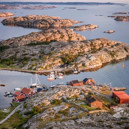 Aerial view of Gothenburg archipelago showing rocky islands with red wooden buildings, boats moored in calm waters, and granite cliffs.