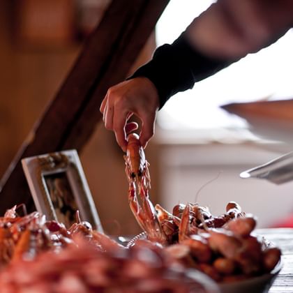 Person selecting fresh cooked crabs and lobsters from a seafood buffet display. Red-orange shellfish are arranged on a wooden surface.