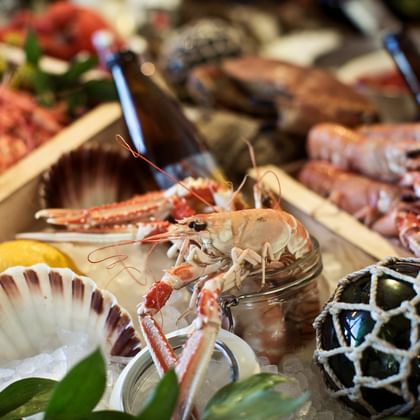 Skaldjursbuffé med färska languster, pilgrimsmusslor och blåmusslor i träboxar på is, garnerad med limeklyftor.