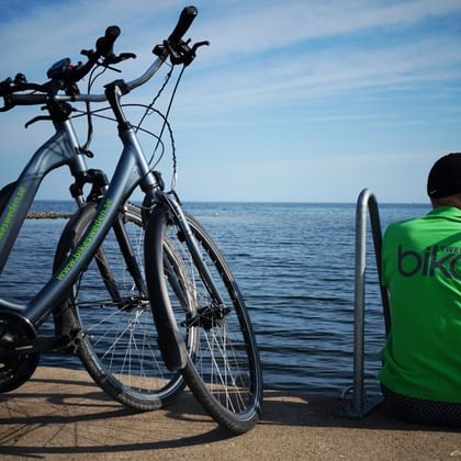 Cyklist i grön tröja tittar på havet från en brygga i Ljugarn, med två parkerade cyklar bredvid under blå himmel.